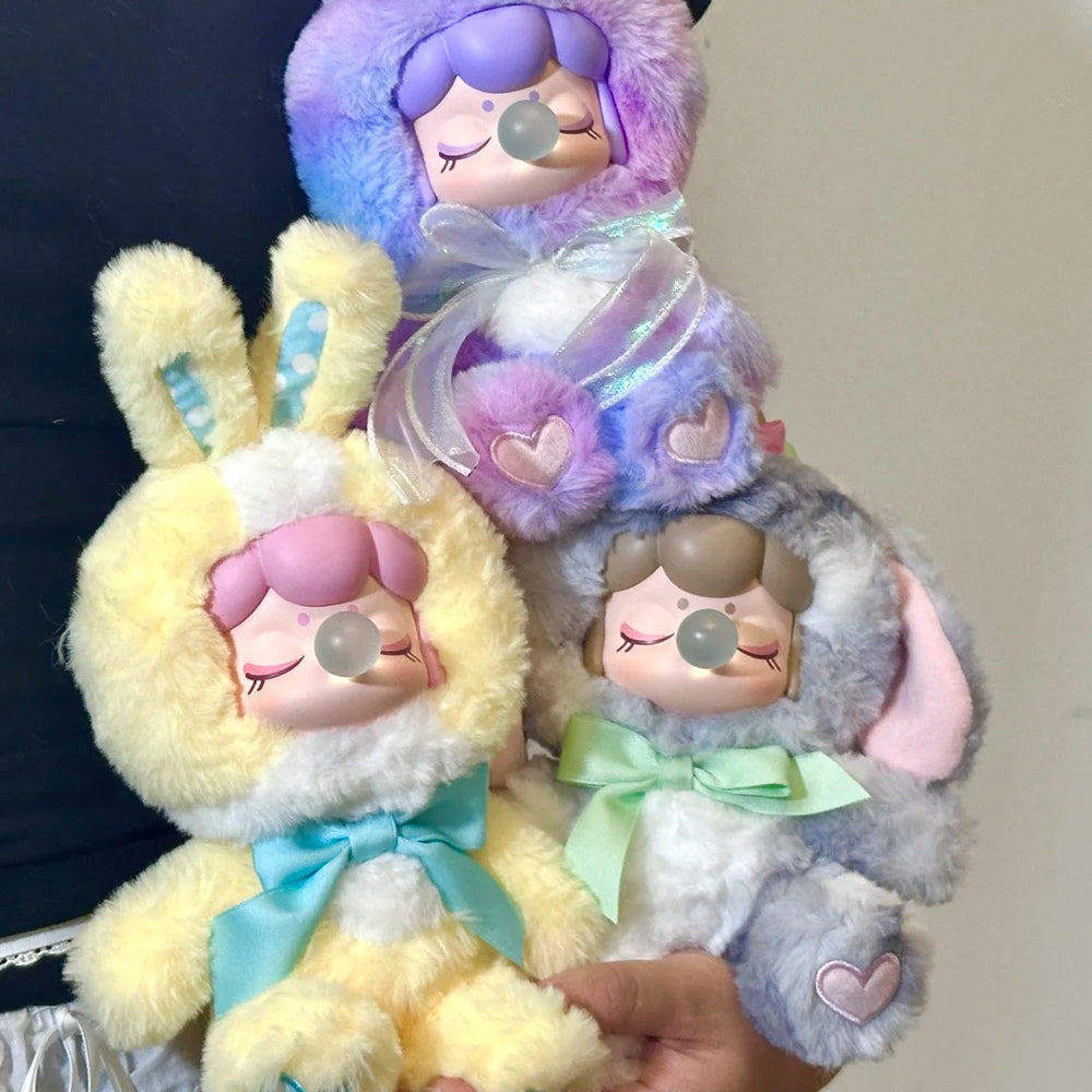 A hand holding three Rolife fluffy bunny plush figures in yellow blue and purple