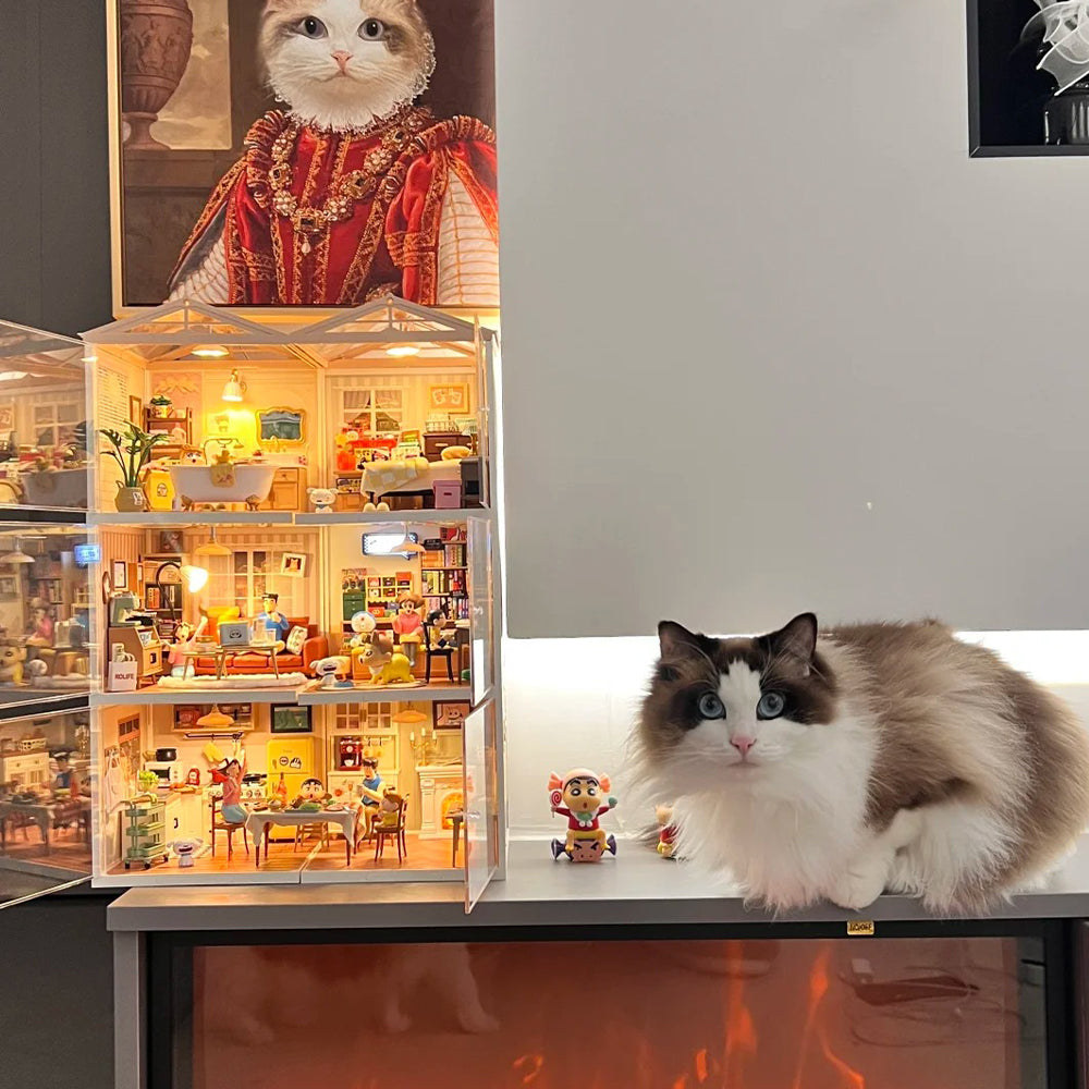 Ragdoll cat sitting beside a lit Rolife Super Creator dollhouse positioned on a mantelpiece, cozy home setting.