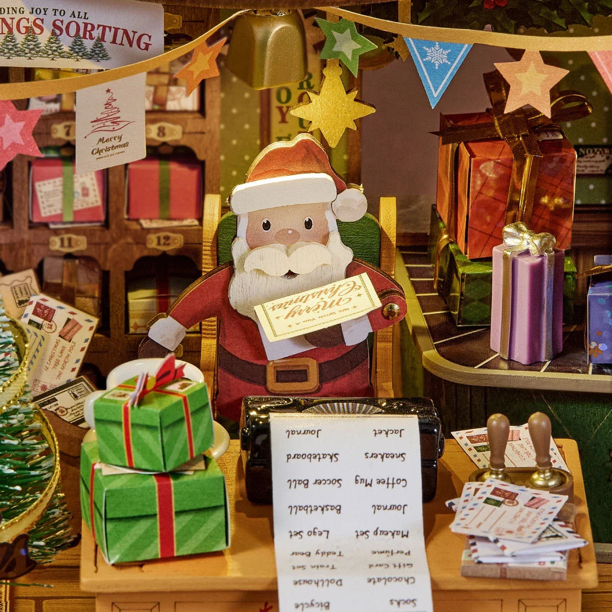 Nahaufnahme einer hölzernen Weihnachtsmannfigur mit Merry Christmas Karte an einem Schreibtisch mit Liste, grün verpackten Geschenken, Briefen und festlicher Wimpelkette im Miniaturpostamt.