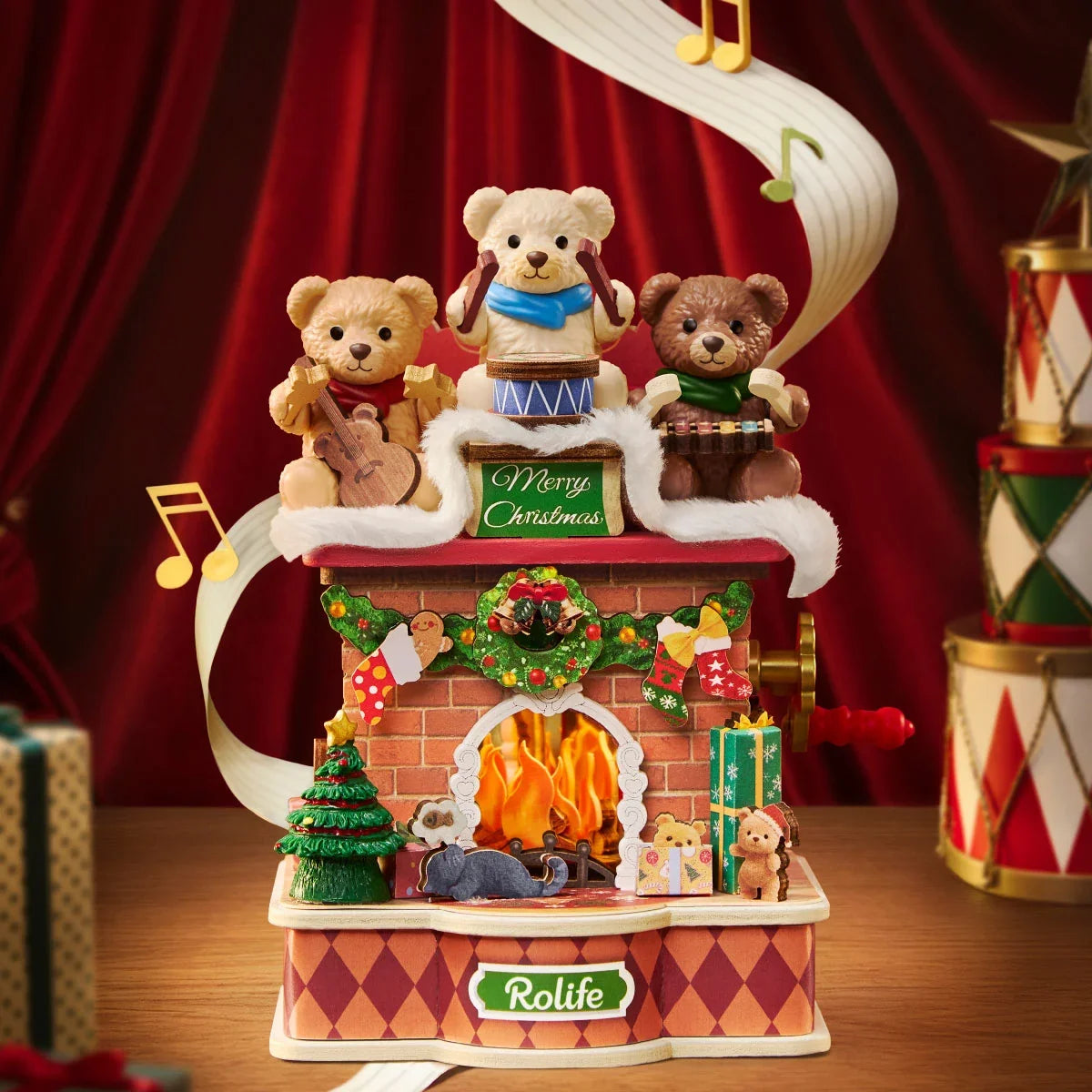Musikalischer Rolife-Weihnachtsziegelkamin mit drei Teddybären, die auf einem verschneiten Dach Gitarre, Trommel und Xylophon spielen, beleuchtetem Kamin, Miniaturbaum und Geschenken vor rotem Vorhang.