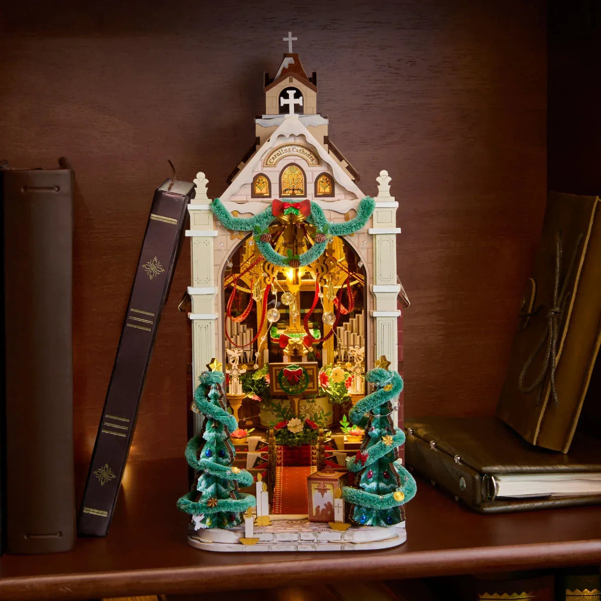 Rolife-Weihnachtskathedrale im Miniaturformat zwischen aufrechten Büchern auf einem Holzregal, mit warm beleuchtetem Bogeninnenraum.