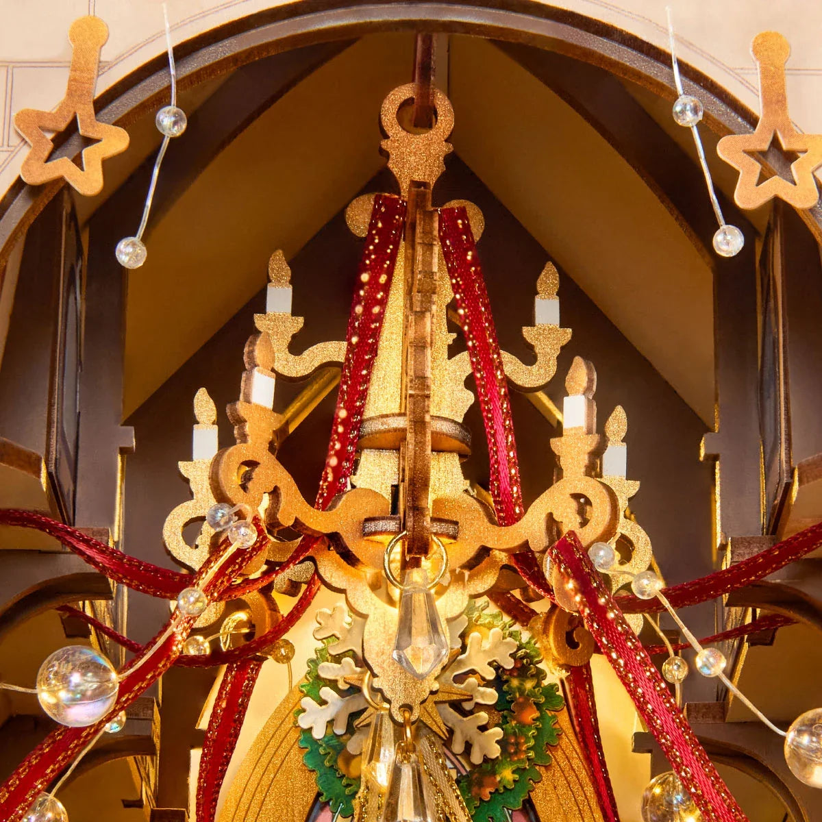 Nahaufnahme des Miniaturkathedralen-Innenraums mit goldenem Kronleuchter in Kerzenform, roten Bändern, klaren Perlen und grünem Kranz.