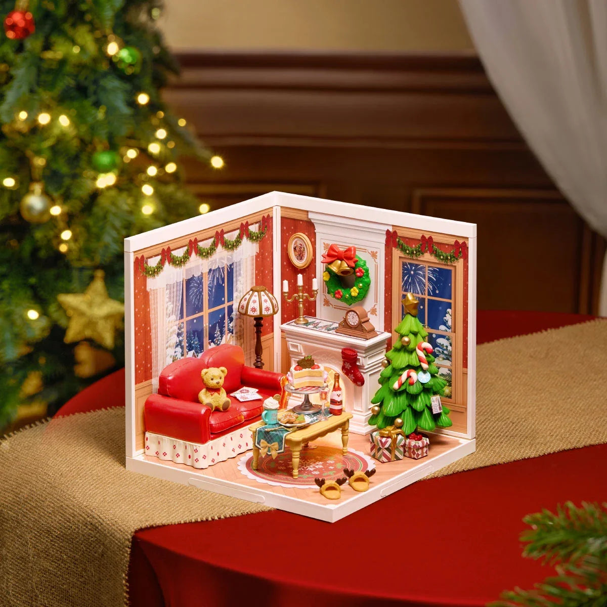 Rolife-Miniaturdiorama eines Weihnachtswohnzimmers auf rotem Tischläufer, mit rotem Sofa, Kamin, Weihnachtsbaum und beleuchteten Fenstern.